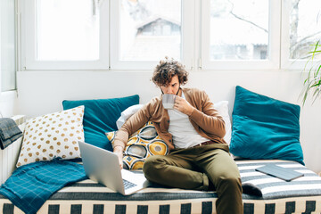 Man sitting on couch drinking coffee and using laptop