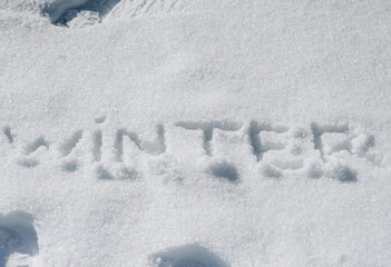 The word winter is written, drawn on white fresh snow. Photo, top view.