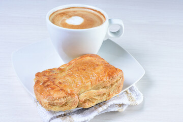 Cup of Colombian coffee, accompanied by baked bakery on white wooden background