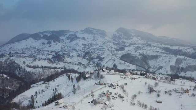 4K Aerial view of Pestera village from Rucar-Bran Pass in Romania during a winter morning at the bottom of Piatra-Craiului Mountains with traditional old houses