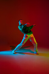 Fototapeta na wymiar Freedom. Stylish sportive boy dancing hip-hop in stylish clothes on colorful background at dance hall in neon light. Youth culture, movement, style and fashion, action. Fashionable bright portrait.