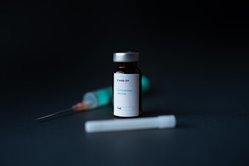 A vial of coronavirus vaccine, a syringe with a needle, with a black background.