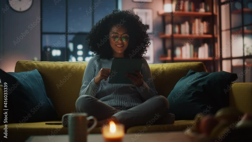 Poster beautiful authentic latina female sitting on couch sofa in a cozy dark living room in the evening an