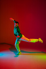Fototapeta na wymiar Freedom. Stylish sportive boy dancing hip-hop in stylish clothes on colorful background at dance hall in neon light. Youth culture, movement, style and fashion, action. Fashionable bright portrait.