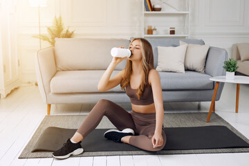 Woman drinking water at the home. Muscular woman taking break after exercise.