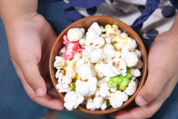 top view of child girl hand holding a bowl of colorful popcorn 