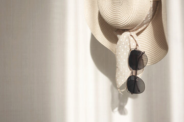 Women straw hat and sunglasses hang on background white wall with shadow. Summer beach fashion...