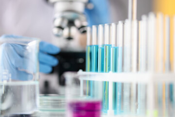 Test tubes with blue liquid standing against background of microscope closeup