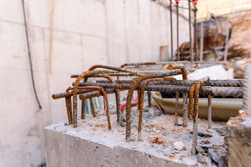 Detail of steel bars inside cement for the reinforced concrete of the foundations of a wall of a building under construction, with unfocused background.