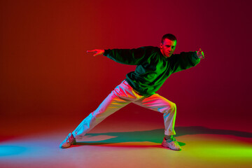 Fototapeta na wymiar Style. Stylish sportive boy dancing hip-hop in stylish clothes on colorful background at dance hall in neon light. Youth culture, movement, style and fashion, action. Fashionable bright portrait.