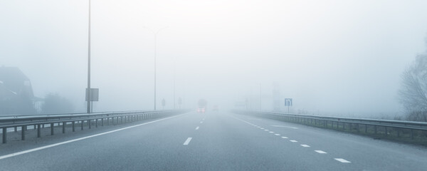 Driver POV on almost empty blue foggy misty rainy highway intercity road with low poor visibility on cold spring autumn morning. Seasonal bad rainy weather accident danger warning. car fog light