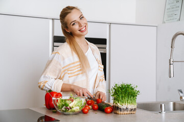Joyful blonde woman smiling while preparing fresh salad