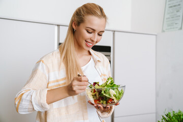 Obraz na płótnie Canvas Joyful blonde woman smiling while preparing fresh salad
