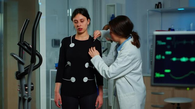 Scientist researcher preparing woman patient for endurance test attaching electrodes on professional body equipment. Team of doctors monitoring health of patinet, vo2, ekg scan runs on computer screen
