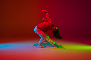Freedom. Stylish sportive girl dancing hip-hop in stylish clothes on colorful background at dance hall in neon light. Youth culture, movement, style and fashion, action. Fashionable bright portrait.