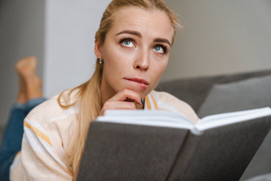 Focused beautiful woman reading book while lying on couch at home