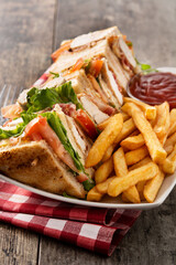 Club sandwich and French fries with ketchup sauce on wooden table