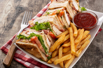 Club sandwich and French fries with ketchup sauce on wooden table