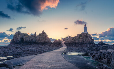 Road to La Corbiere lighthouse on the sea bottom in a low tide with cliff and sunset,  bailiwick of Jersey, Channel Islands