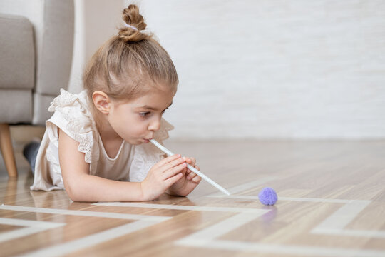 Child little girl playing homemade game with straw and pom pom for better articulation.