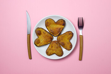Heart-shaped fried potatoes. Fried potatoes in a white plate on a pink background. Love of food