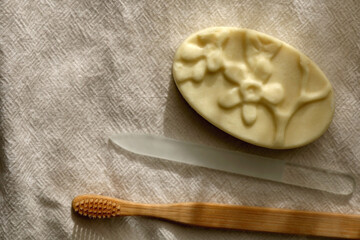 Sustainable toiletries on linen cloth: wooden toothbrush, glass nail file and soap bar. Top view.