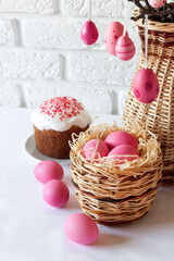 Fototapeta na wymiar Easter composition with decorated tree branches in a wicker vase, pink colored eggs in wicker basket and Easter cake