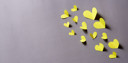 Yellow paper hearts on a gray paper background. Horizontal banner, copy space.