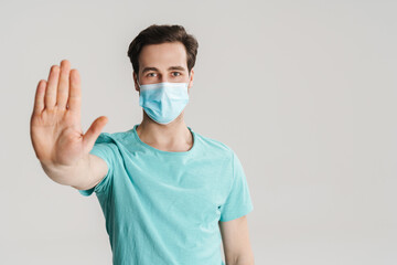 Caucasian handsome guy in protective mask showing stop gesture