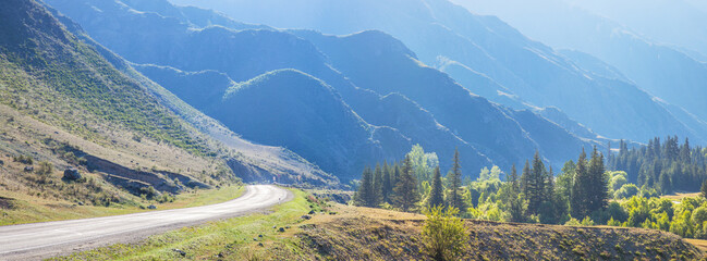 Fototapeta na wymiar Mountain road in summer morning, slopes in blue haze