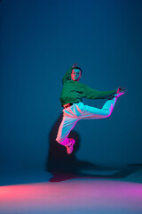 Flying. Stylish sportive boy dancing hip-hop in stylish clothes on colorful background at dance hall in neon light. Youth culture, movement, style and fashion, action. Fashionable bright portrait.