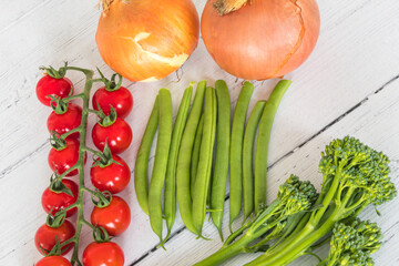 Tenderstem Broccoli Onions Tomatoes and Green Beens laid out on a white painted board from the winter garden.