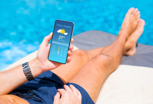 Man relaxing by the pool in hot summer day and checking weather forecast on his mobile phone.