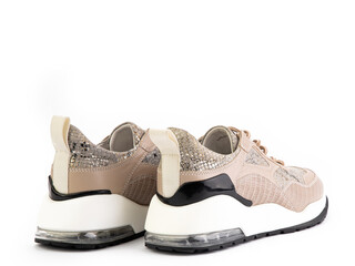 Beige women sneakers that comes in a mix of leather, suede and TPU overlays. Imitation of snake skin. Rubber soles, white on the sides. Isolated close-up on white background. Back side view.
