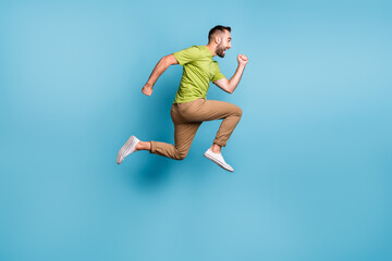 Full size photo of excited man run sale jump up wear brown pants hurry isolated on pastel blue color background