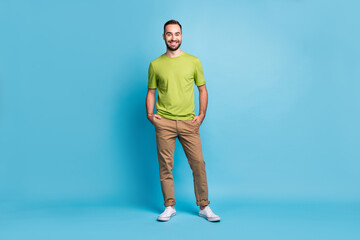 Full size photo of attractive cheerful young brunette man hold hands pockets smile isolated on blue color background