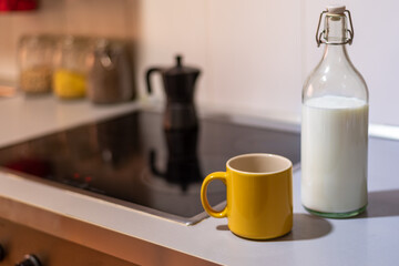 Cup of coffee next to a glass bottle with milk on the kitchen countertop.