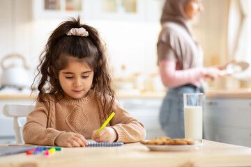 Adorable Little Girl Drawing In Kitchen While Her Muslim Mom Cooking Food