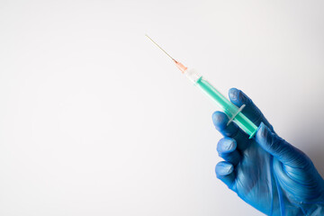 A nurse wearing blue gloves, holding a vial of coronavirus vaccine with one hand, and with the other a needle, with a white background