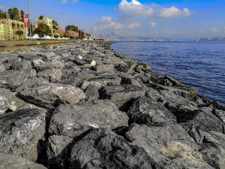 Large gray boulders on the shores of the Bosphorus in Istanbul (Turkey). Beautiful seascape of the sea promenade with the silhouette of the city on the horizon