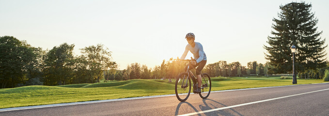 Website header of Rear view of athletic man in sportswear standing with bicycle on the road. Riding...