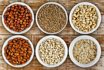 Cashews, peanuts, hazelnuts, almonds, sunflower seeds, pumpkin seeds close up. Nuts in a white bowl on a pink board. Nuts on an old shabby table.