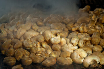 Cashew close up. Texture of nuts. Lots of nuts in a pile. Contrasting dramatic light as an artistic effect. Smoke and steam from roasting seeds in the background.