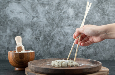 Female hand taking dumpling with chopsticks from plate