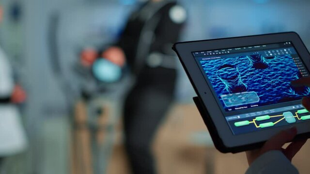 Close up of scientist analysing health informations in tablet while specialist sport supervises exercise of sportsman monitoring his physical endurance. Examining medical scan in notepad in laboratory