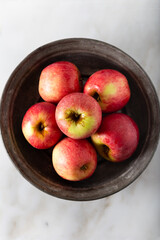 Fresh red apples in rustic plate on white marble background. Top view.