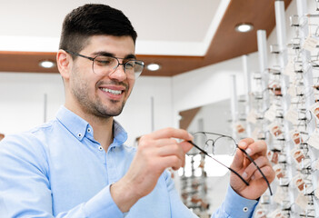 Portrait of happy young male customer choosing eyeglasses