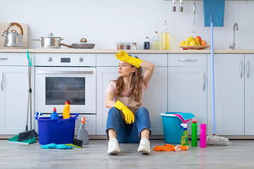 Young housewife tired from domestic work sitting on kitchen floor, wiping her forehead