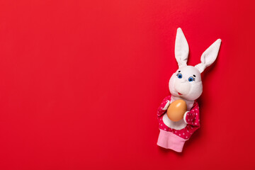 Banner with white bunny and egg in hands on red background with copy space, empty text place. Christian holiday card Happy Easter. Online toy theater course. Hand puppet. Traditional childhood play