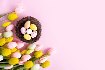 Colorful easter quail eggs in nest and tulips on pink background with . Flat lay. Spring composition. Happy easter greeting card. Copy space